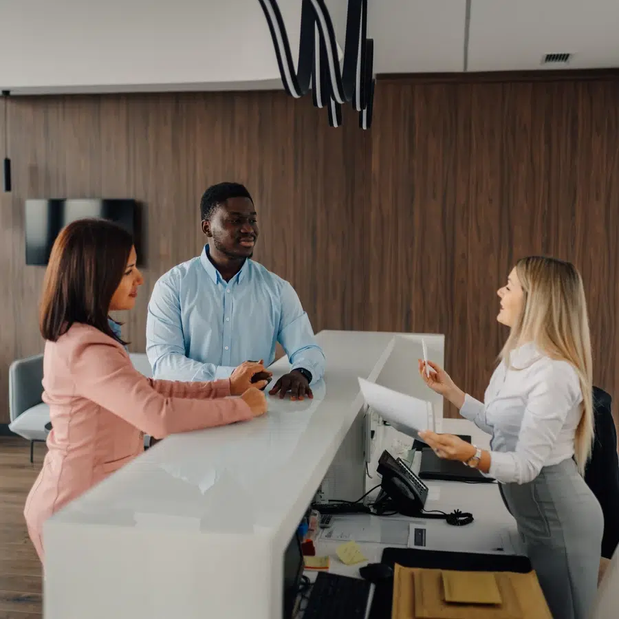 Trois personnes discutent à un comptoir d\'accueil.